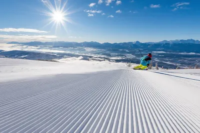 Een skiër op vers geprepareerde piste onder een stralende zon, boven een wolkenzee